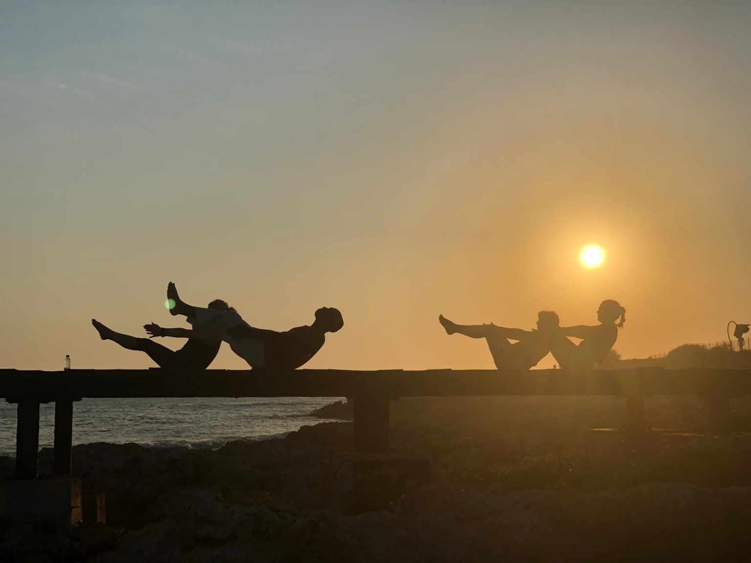 A group practising boat pose silhouetted against the sunset
