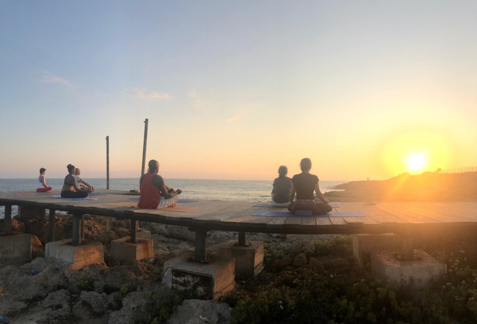 A group seated in meditation beside the sea at sunset